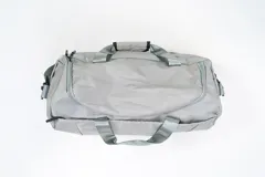 Bolso de viaje gris con doble asa corta y cierre superior. Estampado frontal con la frase "The Tote Bag" en letras blancas.