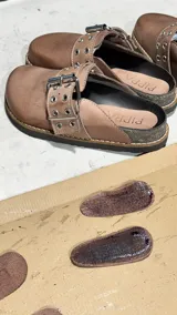 Zueco de cuero color tostado, con hebilla metálica y suela con vira reforzada.