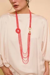 Collar largo de múltiples hilos de cuentas rojas y rosadas, con un dije circular de cuentas y un cierre de mosquetón metálico dorado.
