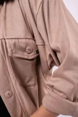 Camisa de estilo sobrecamisa en color beige, confeccionada en tela tipo gamuza o cuero sintético. Presenta cuello clásico, cierre frontal con botones, bolsillos delanteros con solapa y mangas largas con puños abotonados.