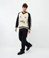 Suéter masculino de punto en modelo boxy, con cuello en V, manga larga y diseño bicolor en beige y negro. Presenta inscripciones bordadas en el pecho, incluyendo la palabra 'Untitled' en tipografía cursiva, y detalles de rayas en los puños, las mangas y el ruedo.