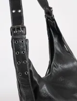 Cartera hobo negra de cuero sintético con costuras blancas decorativas y múltiples cierres diagonales en el frente. Tiene una correa de hombro ajustable.