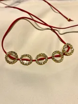 Gargantilla choker con cordón rojo y dijes circulares dorados con strass. El cordón se ata en la parte delantera.
