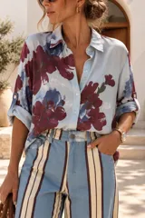 Camisa celestes con estampa de grandes flores borgoña y azules, con cuello camisero, botonadura frontal y mangas largas con presilla para arremangar.