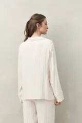 Camisa de pijama color blanco tiza con rayas verticales en relieve, de silueta clásica y caída fluida. Presenta cuello camisero, cierre frontal con botones y detalles de vivo rosado en cuello, puños y solapas.