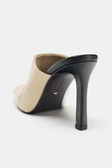 Zapato de tacón tipo mule en piel, de color beige con tacón fino y plantilla en contraste de color negro. Presenta escote redondo, costuras pespunteadas en los laterales y acabado en punta cuadrada.