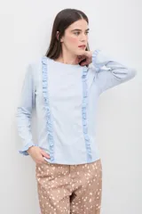Remera de manga larga color celeste, confeccionada en tejido suave con textura acanalada. Presenta volados verticales en el frente y terminaciones con volados delicados en los puños.