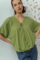 Blusa de lino color fucsia, con escote en V y manga corta amplia. Presenta un detalle de botón decorativo dorado en el centro del escote.