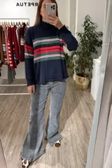 Sweater de punto con cuello alto, manga larga y puños acanalados. Presenta un diseño de rayas horizontales en tonos verde, rojo, negro y blanco sobre una base de color azul marino.