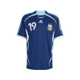 Camiseta de fútbol Adidas de la Selección Argentina, modelo visitante de la temporada 2006. Es de color azul marino con detalles en celeste y blanco, cuello redondo y el número 19 estampado en el frente. Incluye el logo de Adidas y el escudo de la AFA con dos estrellas.