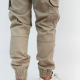 Pantalón cargo color beige de gabardina, con bolsillos laterales y puño en los tobillos.