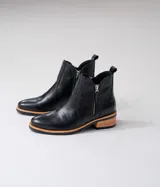 Botas cortas de cuero vacuno color marrón, con diseño de caña baja y cierre metálico en ambos laterales. Presentan un taco cuadrado de madera y suela de goma.