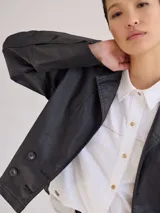 Chaqueta de jean azul oscuro, de corte corto y entallado, con cuello y solapa, y botones de madera en el frente.