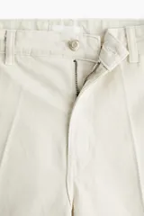 Jean barrel high ankle de denim de algodón rígido color beige, con diseño curvo en las piernas, tiro alto, pliegues delanteros y traseros, y cierre de botón y cremallera.