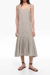Vestido midi con estampado de cuadros vichy en tonos beige y azul, escote en V, tirantes finos ajustables con lazos en los hombros y volante fruncido en el bajo.