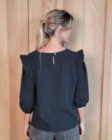Blusa blanca de algodón tussor, con cuello redondo, mangas 3/4 abullonadas y detalle de volados en los hombros.