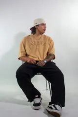 Remera de algodón color beige con corte boxy fit, cuello redondo y mangas cortas. Presenta un diseño bordado en el pecho con la inscripción MTPE.