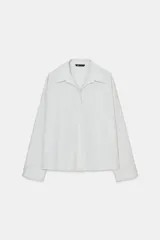 Camisa blanca de popelina con cuello solapa, escote en pico y manga larga con puño. Cierre frontal con botones.