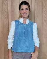 Chaleco de corte recto y largo a la cintura, confeccionado en denim con estampado de rayas verticales en tonos azul y blanco. Presenta cuello redondo y costuras visibles que definen su estructura.