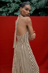 Vestido midi de corte globo con estampado de rayas verticales, cuello halter anudado, escote en pico y espalda descubierta. Presenta bajo abullonado con elástico interior y cierre lateral con cremallera oculta.