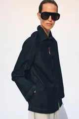 Chaqueta de denim azul oscuro con cuello solapa, manga larga y cierre frontal mediante alamares decorativos de estilo oriental.