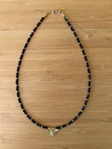 Collar corto de cuentas facetadas negras y detalles dorados, con dije de abeja dorada.