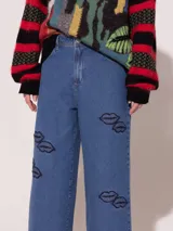Pantalón de jean azul de corte ancho, tiro medio alto y largo a la altura del tobillo. Presenta apliques bordados con forma de labios.
