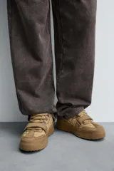 Zapatilla estilo skate de diseño robusto, confeccionada en una combinación de piezas de gamuza y material textil acolchado. Presenta un sistema de cierre con cordones gruesos y una tira de velcro en el empeine, junto con una suela de plataforma con relieve irregular.