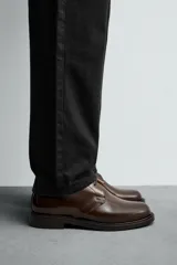 Bota de caña baja tipo chukka, confeccionada en piel con acabado brillante. Presenta cierre de cordones, horma redonda y suela a contraste con ligero tacón.