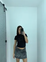 Mini falda de jean con efecto lavado ácido en tonos grises, de tiro bajo y corte recto. Presenta cierre frontal con botones y diseño de cintura asimétrica.