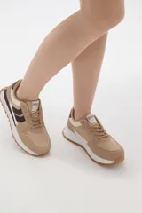 Zapatilla deportiva de diseño urbano, combinando paneles de tela blanca y gamuza sintética en tono gris claro. Cuenta con cordones grises, suela de plataforma con entresuela blanca y base dentada en color caramelo.