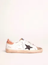 Zapatillas urbanas Golden Goose modelo Super-Star, de cuero blanco con detalles en marrón y estrella negra con glitter en el lateral. Diseño con efecto desgastado en la suela y cordones.