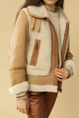 Campera tipo gamulán de cuero en color camel con interior y detalles de piel sintética en color beige. Presenta cierre frontal, bolsillos laterales con cierre y puños con tejido acanalado.