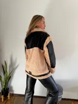 Campera color beige con detalles en negro de piel sintética con cuello y solapas amplias, cierre frontal con cremallera y bolsillos laterales.