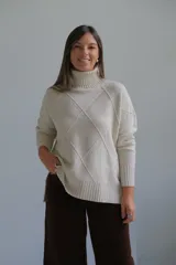 Polerón de cuello alto con diseño de rombos tejidos en relieve, mangas largas con puños acanalados y ruedo asimétrico con aberturas laterales.