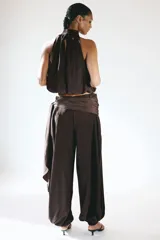 Pantalón de tiro alto color bordó con leve brillo, cintura cruzada con detalle de lazo lateral y piernas estilo globo con elásticos en los tobillos.