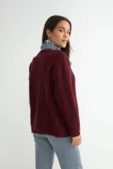 Cardigan de punto con diseño de trenzas, color beige, con escote en V, cierre frontal de botones negros y mangas largas con puños acanalados.