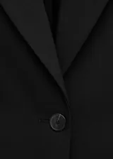 Blazer negro entallado de diseño largo con cuello de solapa y un solo botón de cierre. Cuenta con bolsillos frontales con solapa y una silueta entallada en la cintura.