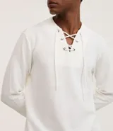 Bata masculina de manga larga en color blanco, confeccionada en tejido texturizado de algodón y poliéster. Presenta cuello en V con detalle de cordones cruzados y lazo ajustable.