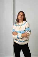 Buzo tejido de punto con diseño de guardas geométricas en tonos celeste y negro sobre base color crema. Presenta cuello redondo, mangas largas y puños acanalados.