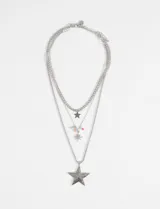 Collar de tres cadenas plateadas superpuestas con dijes de estrella. La cadena más corta tiene un dije de estrella pequeña, la cadena intermedia tiene cuentas de colores y un dije de estrella facetada, y la cadena más larga tiene un dije de estrella grande y facetada.