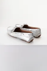 Mocasines plateados de cuero con cordones decorativos y suela de goma marrón.