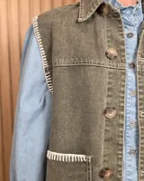 Chaleco de denim color marrón, confeccionado en 100% algodón, con bolsillos frontales amplios, cierre de botones y costuras decorativas bordadas en blanco en los bordes y los bolsillos.