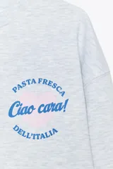 Sudadera de cuello redondo y manga larga, confeccionada en tejido gris melange. Presenta un diseño estampado en el pecho con un corazón y la frase 'Pasta fresca Ciao cara! Dell'Italia'. Cuenta con puños y ruedo acanalados.