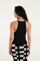 Top tipo musculosa de tejido acanalado blanco, con escote cuadrado y ribetes negros en el borde del escote y las sisas. Presenta doble tirante fino negro.