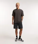 Bermuda de jeans de hombre, color negro con efecto desgastado o acid wash, de corte holgado. Posee cintura elástica con cordón de ajuste y bolsillos laterales.