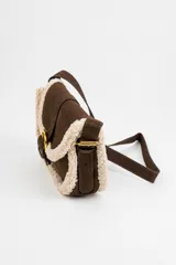 Cartera bandolera marrón de gamuza sintética con detalles de corderito sintético color beige en los bordes. Cuenta con una solapa frontal con cierre de hebilla metálica dorada y correa ajustable.