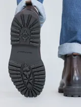 Botín Chelsea para hombre, color marrón oscuro con acabado lustroso, confeccionado en cuero. Presenta paneles elásticos laterales y suela de goma gruesa y dentada.