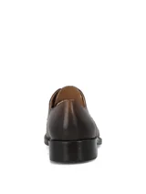 Zapato formal de cuero en color marrón coñac, estilo Oxford con cordones, punta redondeada con costura en la puntera y suela con tacón bajo.