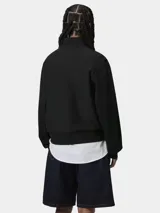 Buzo de cuello alto con cierre frontal parcial, confeccionado en tejido de algodón y poliéster. Presenta un diseño de corte holgado con puños y ruedo acanalados, y el logo de la marca bordado en el pecho.